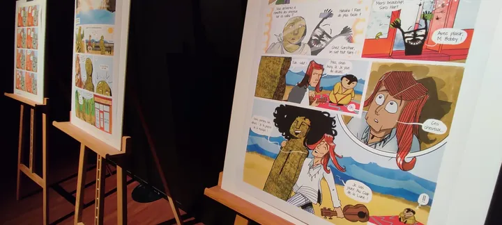 Les planches de la bande dessinée collective exposées sur des chevalets.